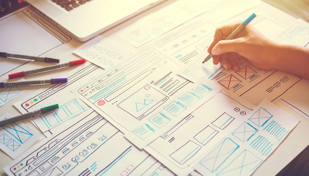 A person drawing web design concepts using markers on sheets of paper